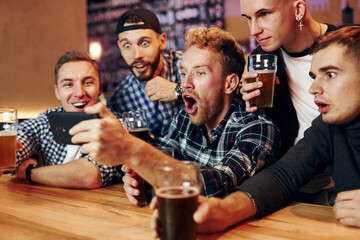 Uses phone. Group of people together indoors in the pub have fun at weekend time