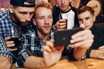 Uses phone. Group of people together indoors in the pub have fun at weekend time