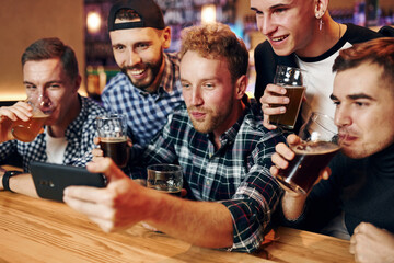 Uses phone. Group of people together indoors in the pub have fun at weekend time