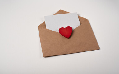 Craft envelope with a blank sheet of paper inside and red wooden heart on the white background. Romantic love letter for the Valentine's day concept. Space for text.