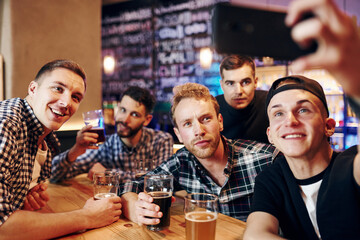 Man takes selfie by phone. Group of people together indoors in the pub have fun at weekend time