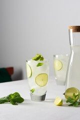 Refreshing cold drinks with lime and mint, glasses with lemonade and ice, jug with drink on white...