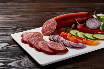 Sausages with a garnish of vegetables and herbs with sauces and bread on a white rectangular plate on a dark wooden table.