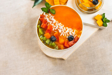 Fresh fruit breakfast. Smoothie bowl of mango, papaya on the table, decorated with pieces of kiwi, blueberry berries and mint leaf