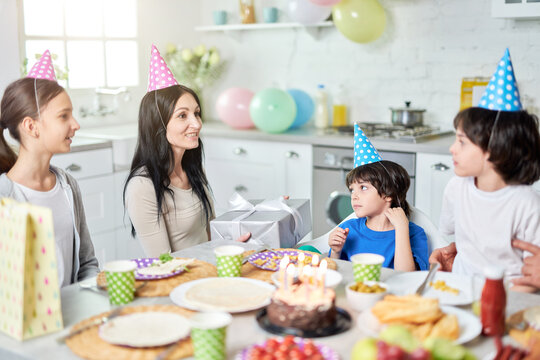 Family party. Cheerful middle aged latin mother holding gift box, talking to her lovely children while having dinner, celebrating birthday together at home