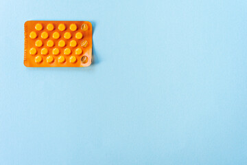 Orange blister with three tablets already taken. Blister pack of medication isolated on light blue background. Top view angle.