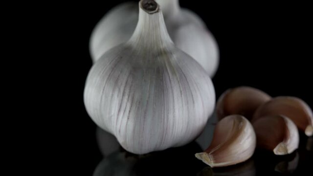 organic garlic on black table, closeup view, rotating bulb and clove