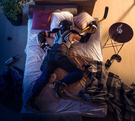 Fototapeta na wymiar Champion. Top view of young professional hockey player sleeping at his bedroom in sportwear with equipment. Loving his sport, workaholic, playing match even if resting. Action, motion, humor.