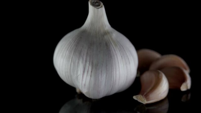 bulb and cloves of garlic on black background in studio, closeup view, rotating