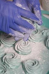 Woman in rubber gloves makes marshmallows. Sprinkles it with powdered sugar. Dessert lies on the table surface.