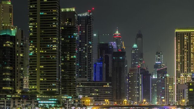Promenade in Dubai Marina timelapse at night, UAE. Top view with palms, boats and towers. District with artificial canal and illuminated skyscrapers