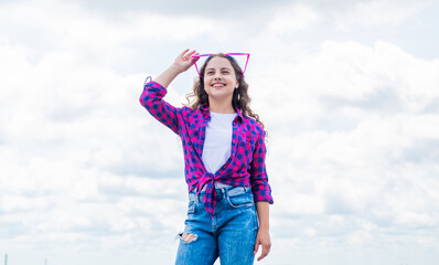 Fototapeta na wymiar hair beauty and care. kid fashion style. teenage girl on sky background outdoor. hipster kid. happy childrens day. happy childhood. smiling child with party glasses