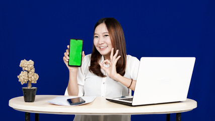 business Asian woman with green screen handphone in workspace isolated blue background