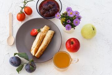 Homemade pancakes filled with cottage cheese on a plate, fruits and a cup of tea