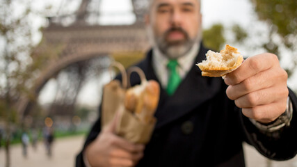 Handsome man wearing suit and coat eating a french roll over Eiffel tower