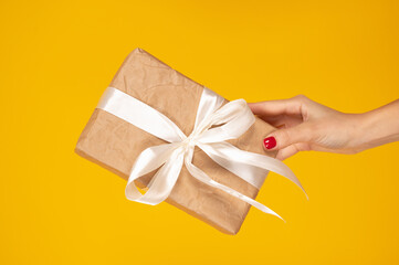 Cropped hand of woman holding wrapped gift box over yellow background. Holidays postcard concept