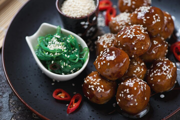 Close-up of roasted meatballs in teriyaki sauce with sesame seeds and seaweed salad, selective focus