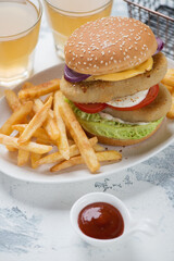 Double burger with sesame bun, fish cutlets, vegetables and french fries, vertical shot on a white concrete surface