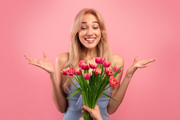 Gorgeous young lady feeling excited to receive bunch of tulips for Woman's Day on pink studio background