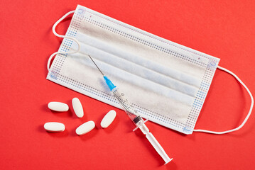 A medical mask, white pills and a vaccine syringe on red background. close-up, macro