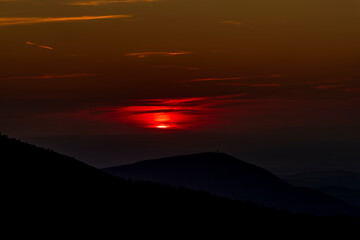 A detailed view of the sun as it changes from yellow to red and slowly sets behind the mountainous area of the Beskydy Peaks and the surrounding nature.
