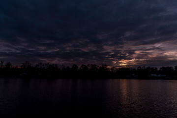 The water surface of the lake during a colorful sunset with the reflection of the surrounding tree on the water surface.