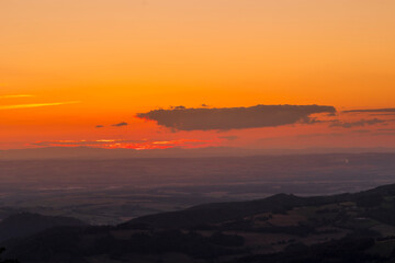 A view of a landscape full of mountains during a golden sunset with the sun on the horizon and a view of the sun from the top of Mount Ondrejnik.