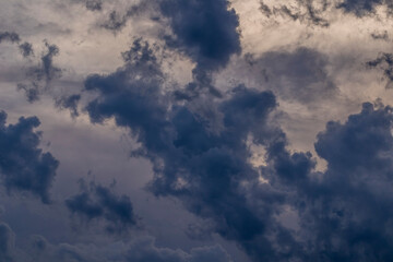 Dark clouds moving in the sky and rapidly changing shapes with the sun in the background at sunset.