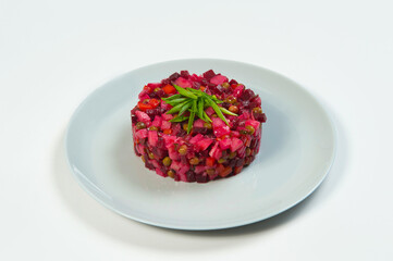Side view of Russian vinaigrette salad of beetroot. Traditional salad with oil and vinegar served with spring onion scallions on gray plate on white background. Salad of boiled vegetables

