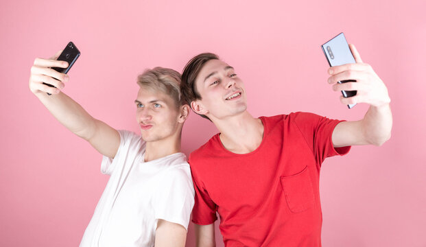 Isolated on pink background two different brunet and blond men making selfie with smartphone camera