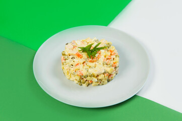 Side view of Russian traditional holiday Olivier salad. Dish of boiled vegetables dressed with mayonnaise sauce. Christmas New Year cold dish served on gray plate on green colorful abstract background