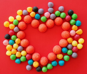 Colorful dragee beans in the shape of a heart on a red background. Decoration background. Closeup.

