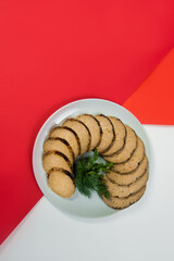 Top view of Stuffed carp fish. Vertical shot of Jewish traditional gefilte fish slices served with fresh green herbs - dill and parsley on red and white abstract background Minced fish with vegetables
