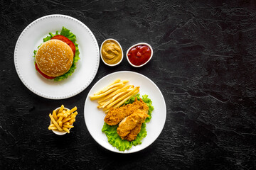 Burger with fried potatoes and chicken, top view