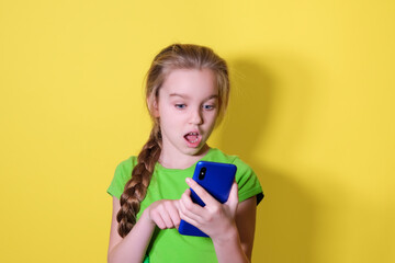 Surprised teenage girl looking at her mobile phone screen. Child girl uses a smartphone