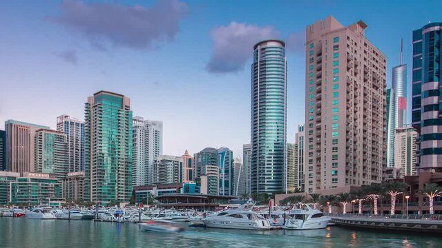 Dubai Marina with towers and yacht club from waterfront in Dubai day to night transition timelapse, United Arab Emirates. District in Dubai and an artificial canal after sunset