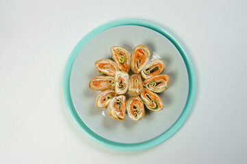 Top view of Holiday Russian starter dish blini with cream cheese, salmon and cucumber. Marinated red fish fillet wrapped in crepes. Seafood appetizer with vegetables served on plate. Isolated object
