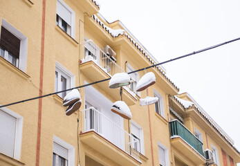 Fototapeta na wymiar Snow covered sneakers hanging from high voltage cables in a Madrid street during “Filomena” storm. 