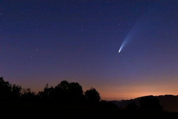 Comet Neowis moving shortly after sunset in a blue sky to the side captured over the mountainous landscape of the Beskydy Mountains. © Lukas