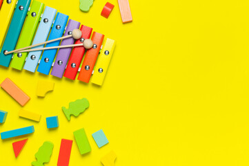 Multicolored wooden xylophone, wooden constructor on yellow background flat lay top view copy space. Wooden children's toy. Baby musical instrument. Colors of rainbow. Kids natural eco toys