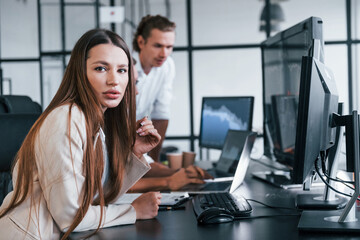 Obraz premium Woman looks into the camera. Team of stockbrokers works in modern office with many display screens