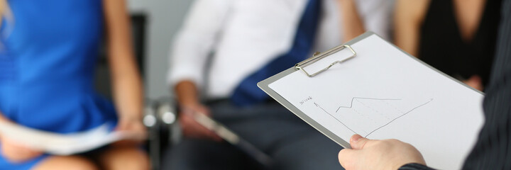Cropped head of male ceo holding financial chart while female and male managers are sitting on...