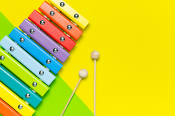 Multicolored wooden xylophone, shock sticks on yellow and green background flat lay top view copy space. Wooden children's musical toy. Baby musical instrument. Colors of rainbow Kids natural eco toys