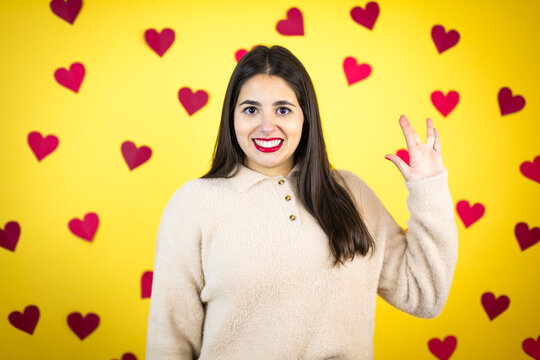 Young caucasian woman over yellow background with red hearts doing star trek freak symbol