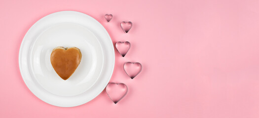 A Burger in the shape of a heart lies beautifully on a white plate.Pink background. Food for the Valentine's Day holiday.the baking forms in the shape of a heart.