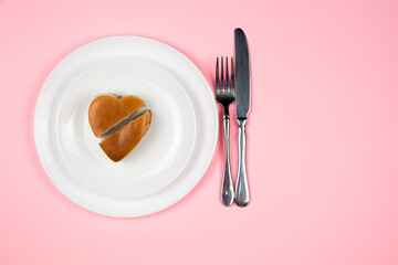 A Burger in the shape of a heart cut open on a white plate.Pink studio background. The view from the top. Concept of Valentine's Day.
