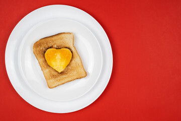 heart shaped breakfast sandwich with egg in the middle on a plate. Red background.