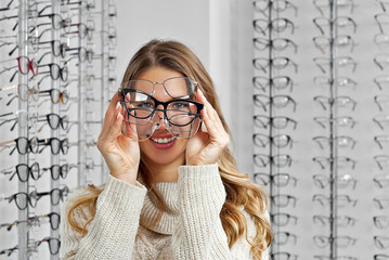 Woman chooses glasses in the store. Blonde in a beige sweater buys glasses. Girl on a background of...