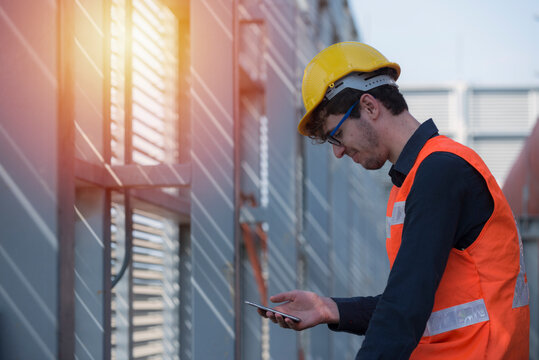 Male Industrial Worker In The Hard Hat Uses Mobile Phone While Walking Through Heavy Industry Manufacturing Factory.