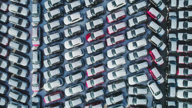 Aerial top down view of new cars parked in car parking lot. Car dealer parking lot full of new automobiles. New cars lined up for import and export business.